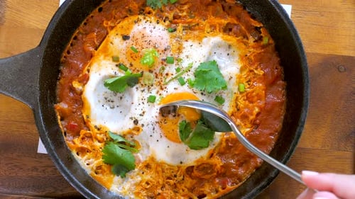 La mano de una mujer toma un shakshouka o un shakshuka de Iron Pan
