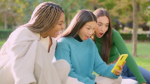 Three Surprised Friends Using a Mobile Sitting Outdoors