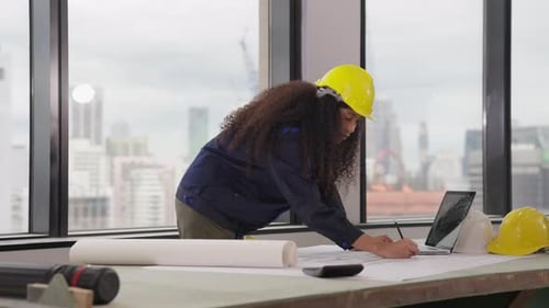 Female Architect with Yellow Helmet Drawing on Blueprint
