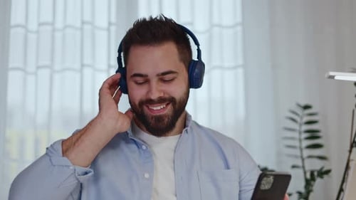 Careless Male in Headset Enjoying Music Application on Cellphone at Home Office