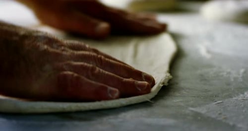 Close up of a pizza chef's hands kneading the dough to prepare a gourmet pizza and spreads the tom