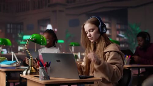 Female Student Studies with Laptop and Headphones in Library