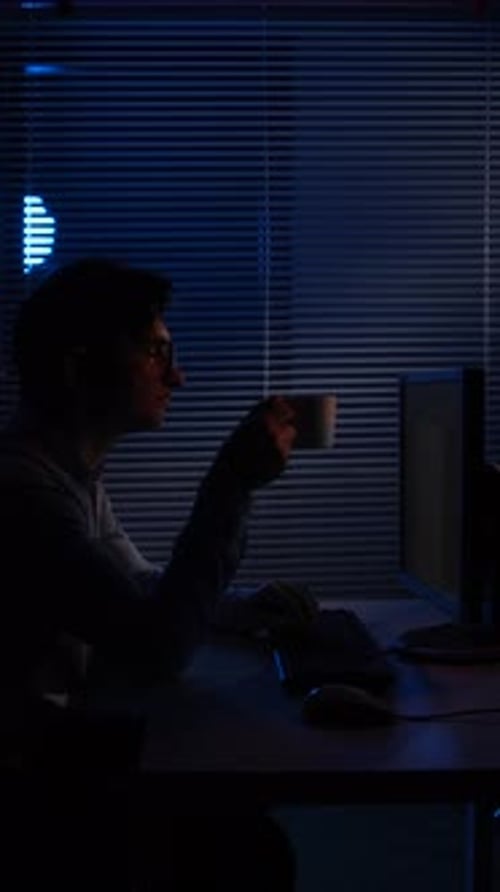 Vertical Video Man in Silhouette Working Late at a Desk By a Blind Covered Window Illuminated By