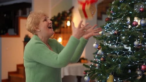 Senior Woman Decorates Christmas Tree with Gift