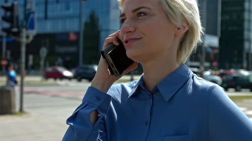 Young business woman in a blue shirt talking in the city center on a mobile phone. In the background
