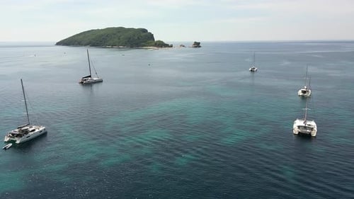 A Drone Flies to an Island in the Adriatic Sea Flying Over Snowwhite Yachts Standing in Turquoise