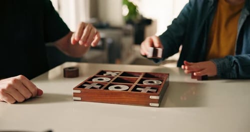 Adults Playing Tic-Tac-Toe Game Indoors at Table