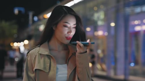 Stylish Woman Uses Voice Command on City Street at Night