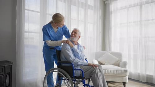 Nurse Comforting Senior Man in Wheelchair Indoors