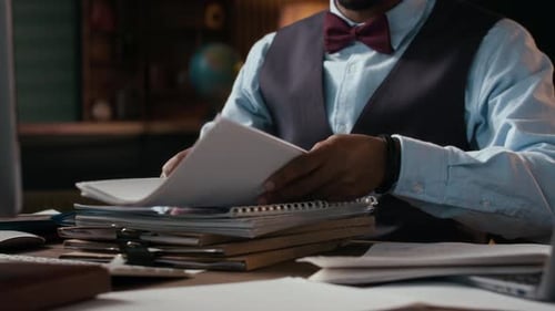Teacher Organizing and Checking Papers at Table in College Office