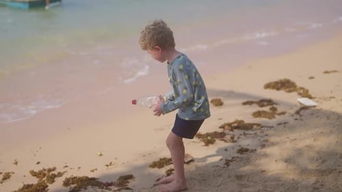 Boy Picks Up Plastic Bottle On The Beach