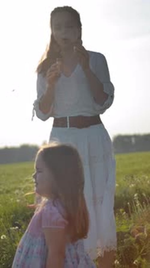 Young Woman and Child Blow Bubbles on Green Field