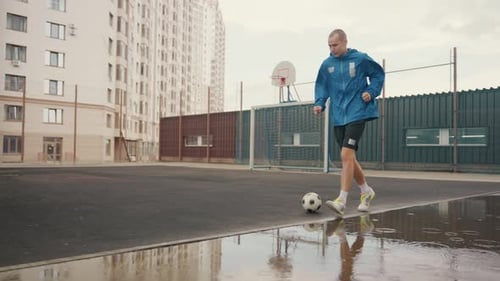 Man Dribbling Soccer Ball on Wet Urban Field