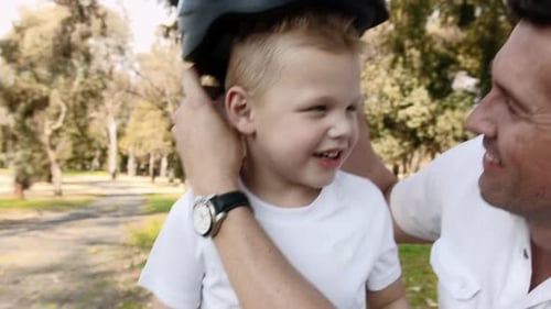 Steadicam Shot Of Father Teaching Son How To Use His His Safety Helmet On A Park Pathway.