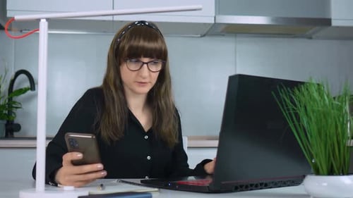 Young Pretty Woman Professional Holds Modern Smartphone in Home Office Texting and Utilizing Helpful