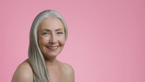 Studio Portrait of Happy Grey Haired Lady with Bare Shoulders Turning Face to Camera and Smiling