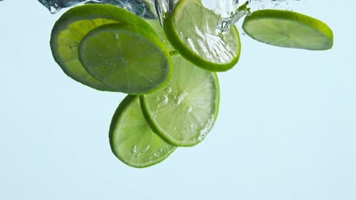 Tropical Sliced Lime Dropped Into Crystal Water White Background Close Up. Pieces