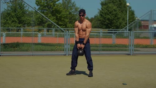 Young Man Training on Outdoor Sports Field and Performs Kettlebell Throw with Both handsExercise to