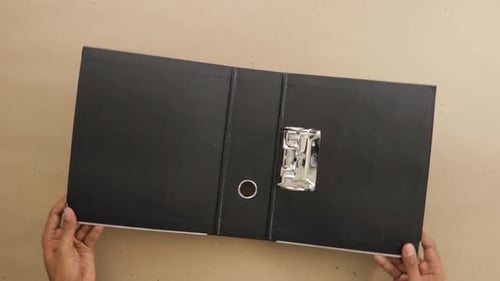 Aufklappbarer schwarzer Aktenordner mit Ringbuch auf dem Schreibtisch.