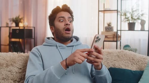Surprised Young Adult Using Smartphone Indoors on Couch