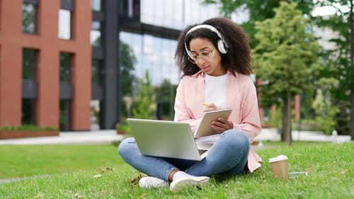 Afroamerikanische Studentin hört sich Online-Videokurs mit Laptop auf dem Rasen an