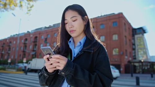 Jeune femme asiatique envoyant des SMS sur smartphone dans la ville
