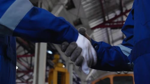 Two Workers in Blue Shake Hands in Factory