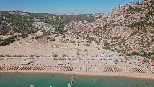Aerial view of a sunny beach with umbrellas and distant mountains in summer