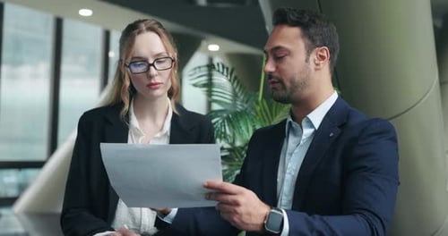Corporate CEO giving feedback to female employee while reviewing project paper documents in office