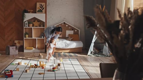 Parent Helps Baby Take First Steps in Playroom