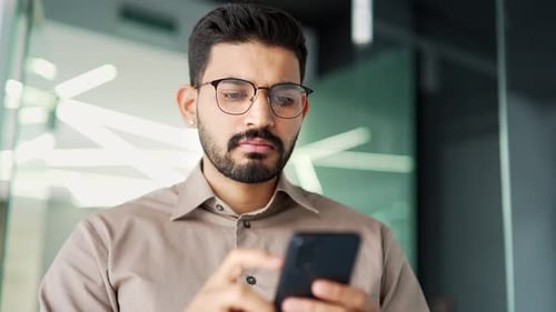 Serious businessman is using smartphone standing in business office. Thoughtful handsome