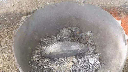 Molten lead being stirred in a metal pot, flames licking the surface, top down view