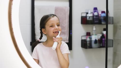 Girl Brushing Teeth with Electric Toothbrush in Bathroom