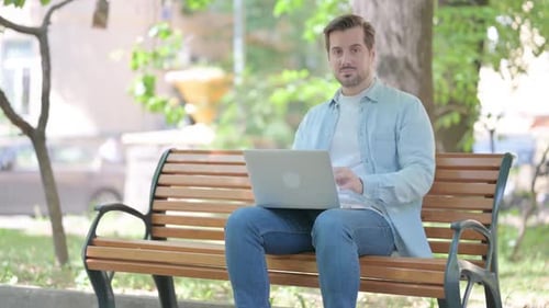 Joven apuntando a la cámara mientras usa una computadora portátil al aire libre