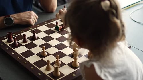Kleines Mädchen spielt Schach mit ihrem Vater am Tisch in der heimischen Küche