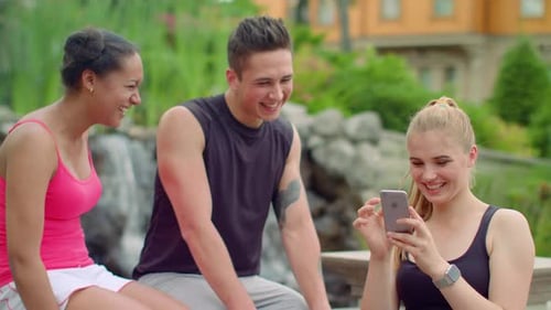 Multiracial friends enjoying a sunny day in the park laughing and using phones