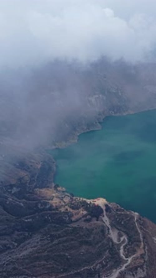 Panorama aérien vertical du cratère volcanique de Quilotoa : nuages brumeux balayant les eaux turquoises