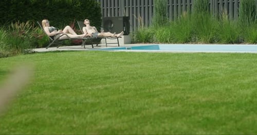 A Young Couple is Relaxing By the Pool in the Backyard of the House In the Foreground a Wellgroomed