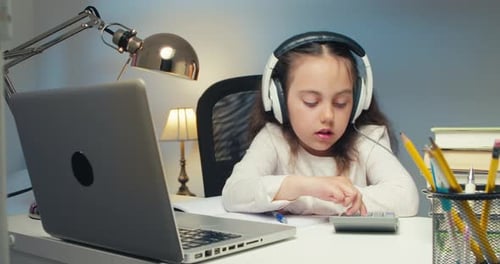 Little Girl in Headphones with a Laptop Studying Online at Home