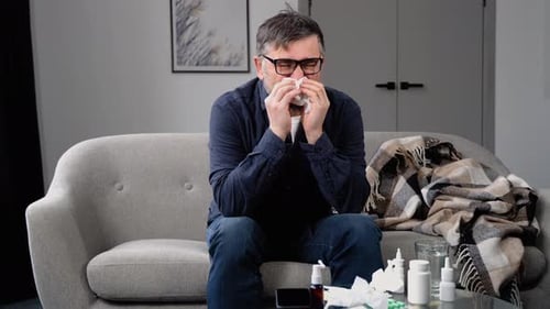 Man With Cold Blowing Nose on Sofa