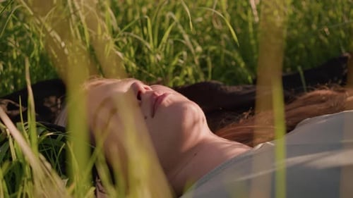 Thoughtful Woman Lying in Sunlit Grassy Field Surrounded By Tall Green Grass