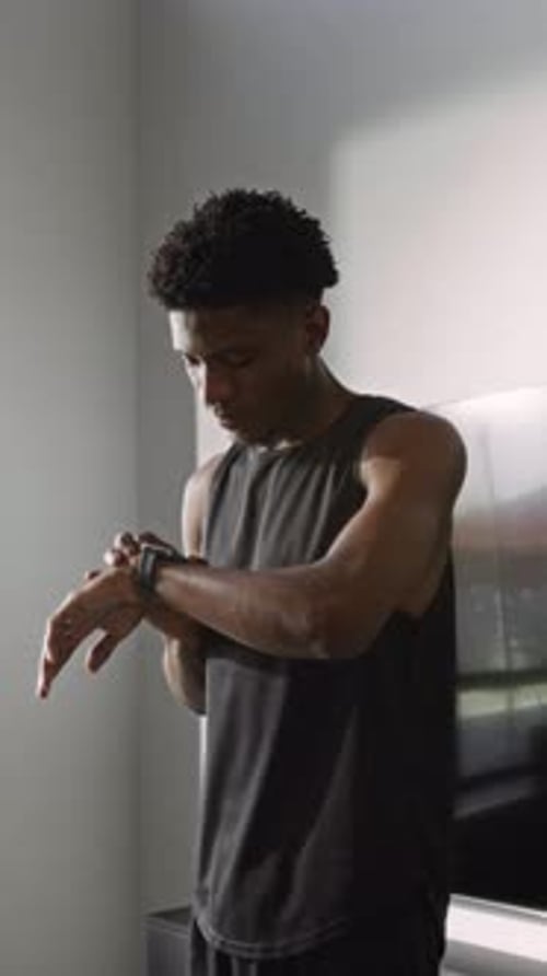 Afroamerikanischer Athlet, der den Timer für das Training einstellt und die Schultergelenke dehnt