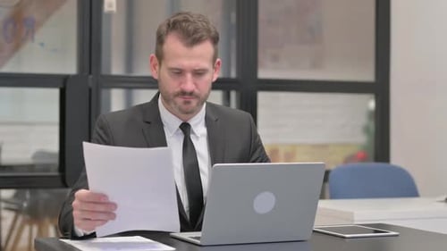 Serious Businessman Reviews Documents at Desk