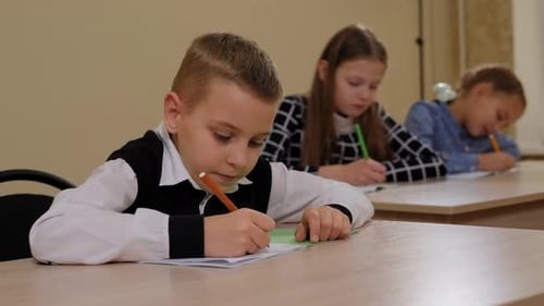 Nahaufnahme eines kleinen Jungen, der in der Schule an einem Schreibtisch sitzt und in ein Notizbuch schreibt
