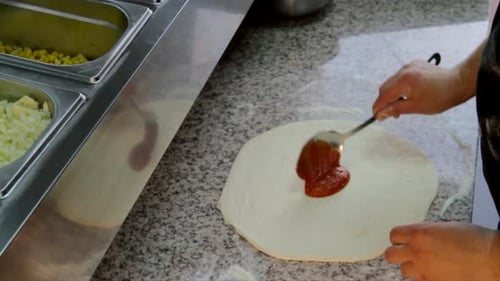 Zubereitung von Pizzabacken. Der Küchenchef trägt Tomatensauce auf den Pizzateig auf.
