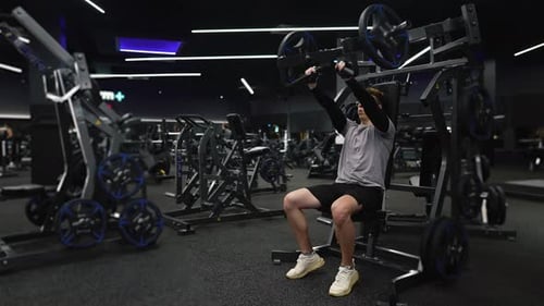 Fitness-Mann trainiert in einem modernen Fitnessstudio und macht eine Übung auf modernen Simulatoren (Push-Zeitlupe)