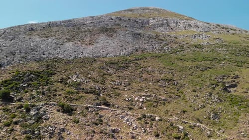 Antenne aérienne montante au-dessus d'une montagne rocheuse arridée avec sentier et ciel bleu