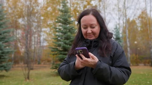 Woman Using Smartphone Browsing Social Media in Autumn Park