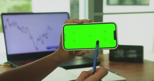A Woman's Hand Phone with Green Mockup Screen Chroma Key Holds a Smartphone of the Workspace