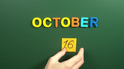 Hand sticking a sticker 16 October calendar day on school board. 16 date of October. Sixteenth day
